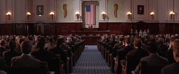 Movie still from “Mars Attacks!” (1996), directed by Tim Burton – A group of people sitting in front of an american flag; Extreme Wide shot, High angle