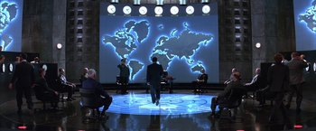 Movie still from “Mars Attacks!” (1996), directed by Tim Burton – A group of people sitting in front of a world map; Extreme Wide shot, High angle