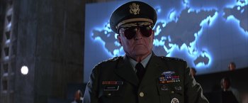 Movie still from “Mars Attacks!” (1996), directed by Tim Burton – An older man in a military uniform wearing sunglasses; Medium shot, Low angle