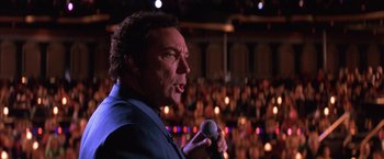 Movie still from “Mars Attacks!” (1996), directed by Tim Burton – A man is speaking into a microphone in front of an audience; Close Up shot, Low angle