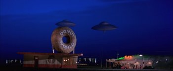 Movie still from “Mars Attacks!” (1996), directed by Tim Burton – A donut world sign in the middle of the night with ufos above it; Extreme Wide shot, Low angle