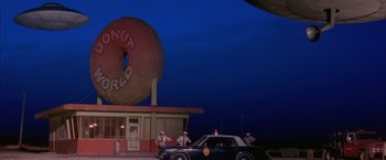 Movie still from “Mars Attacks!” (1996), directed by Tim Burton – A donut shop with a cop car parked in front of it at night; Extreme Wide shot, Low angle