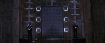 Movie still from “Mars Attacks!” (1996), directed by Tim Burton – Two people are standing in front of a door; Wide shot, Low angle