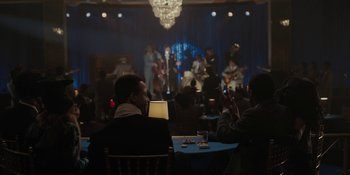 Movie still from “Marshall” (2017), directed by Reginald Hudlin – Two men sitting at a table in front of an orchestra; Wide shot, Over the shoulder angle
