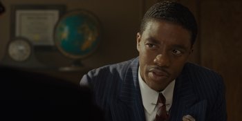 Movie still from “Marshall” (2017), directed by Reginald Hudlin – A man wearing a suit and tie sitting in front of a globe in a room; Close Up shot, Over the shoulder angle