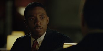 Movie still from “Marshall” (2017), directed by Reginald Hudlin – A man wearing a suit and tie sitting in front of a lamp; Close Up shot, Low angle