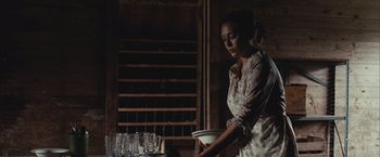 Movie still from “Martha Marcy May Marlene” (2011), directed by Sean Durkin – A woman standing in front of a bunch of wine glasses; Medium shot, Over the shoulder angle