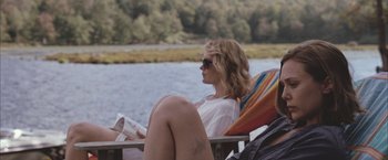 Movie still from “Martha Marcy May Marlene” (2011), directed by Sean Durkin – A woman sitting in a chair reading a book by the water; Medium shot, High angle