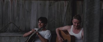 Movie still from “Martha Marcy May Marlene” (2011), directed by Sean Durkin – Two young men sitting next to each other with guitars; Medium shot, Low angle