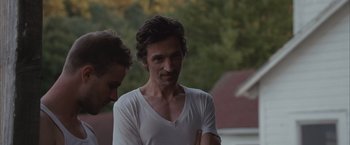 Movie still from “Martha Marcy May Marlene” (2011), directed by Sean Durkin – A man in a white t - shirt standing next to another man; Close Up shot, Over the shoulder angle