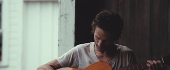 Movie still from “Martha Marcy May Marlene” (2011), directed by Sean Durkin – A man is playing a guitar in a room; Close Up shot, Over the shoulder angle