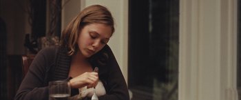Movie still from “Martha Marcy May Marlene” (2011), directed by Sean Durkin – A woman sitting in front of a window holding a pair of scissors; Medium shot, Over the shoulder angle