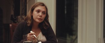 Movie still from “Martha Marcy May Marlene” (2011), directed by Sean Durkin – A woman sitting in front of a window holding a remote control; Close Up shot, Over the shoulder angle