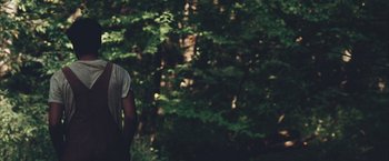 Movie still from “Martha Marcy May Marlene” (2011), directed by Sean Durkin – A man standing in front of a forest with trees in the background; Medium shot, Over the shoulder angle