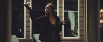 Movie still from “Martha Marcy May Marlene” (2011), directed by Sean Durkin – A woman standing in front of a window holding a white object; Medium shot, Low angle