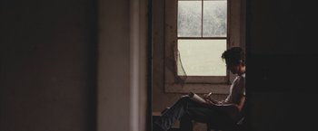 Movie still from “Martha Marcy May Marlene” (2011), directed by Sean Durkin – A man sitting in front of a window reading a book; Medium shot, Over the shoulder angle