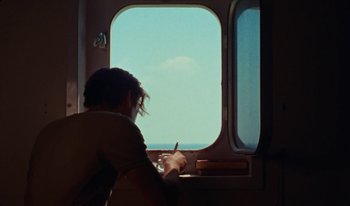 Movie still from “Martin Eden” (2019), directed by Pietro Marcello – A person sitting in front of an open window on a boat; Medium shot, High angle