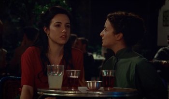 Movie still from “Martin Eden” (2019), directed by Pietro Marcello – Two women are sitting at a table with drinks in front of them; Medium shot, Over the shoulder angle