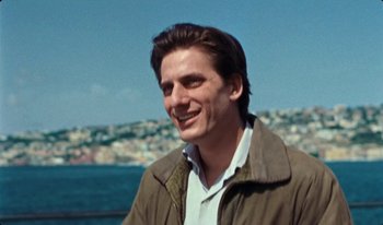 Movie still from “Martin Eden” (2019), directed by Pietro Marcello – A young man smiling for the camera near the ocean; Close Up shot, Low angle