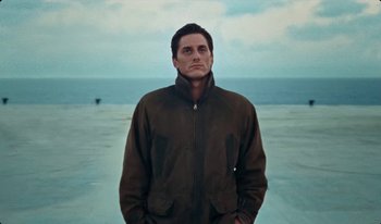 Movie still from “Martin Eden” (2019), directed by Pietro Marcello – A man standing on the beach wearing a brown jacket; Medium shot, Low angle