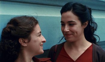 Movie still from “Martin Eden” (2019), directed by Pietro Marcello – Two young women smiling and looking at one another; Close Up shot, Over the shoulder angle