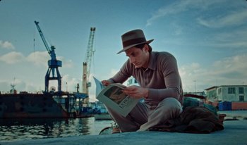 Movie still from “Martin Eden” (2019), directed by Pietro Marcello – A man sitting on the ground while reading a magazine; Medium shot, Low angle