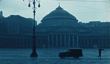 Movie still from “Martin Eden” (2019), directed by Pietro Marcello – A car driving down a street in front of a large building; Extreme Wide shot, Low angle