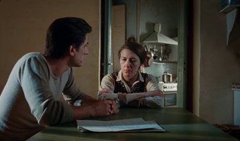 Movie still from “Martin Eden” (2019), directed by Pietro Marcello – Two people sitting at a table in front of a stove; Medium shot, Over the shoulder angle