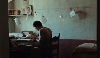 Movie still from “Martin Eden” (2019), directed by Pietro Marcello – A man sitting at a table looking at his phone; Medium shot, Low angle