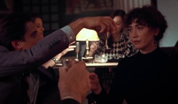 Movie still from “Martin Eden” (2019), directed by Pietro Marcello – A man is handing a glass to another man; Medium shot, Over the shoulder angle