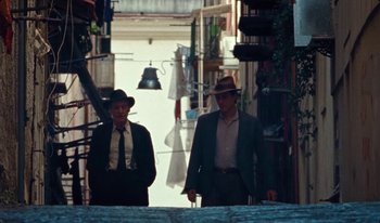 Movie still from “Martin Eden” (2019), directed by Pietro Marcello – A couple of people that are standing in the street; Wide shot, Low angle