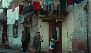 Movie still from “Martin Eden” (2019), directed by Pietro Marcello – A man holding an umbrella while standing next to a building; Wide shot, Low angle