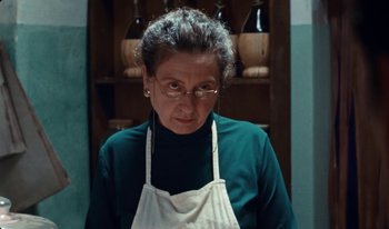 Movie still from “Martin Eden” (2019), directed by Pietro Marcello – An older woman wearing glasses and an apron in a kitchen; Close Up shot, Low angle