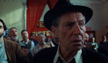 Movie still from “Martin Eden” (2019), directed by Pietro Marcello – An old man wearing a black hat in front of a crowd; Close Up shot, Low angle