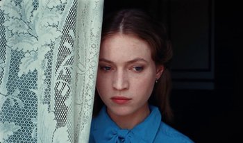 Movie still from “Martin Eden” (2019), directed by Pietro Marcello – A young woman in a blue shirt is behind a lace curtain; Close Up shot, High angle