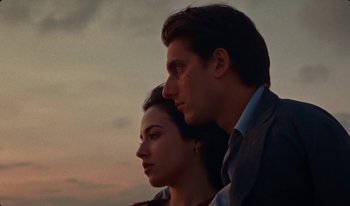 Movie still from “Martin Eden” (2019), directed by Pietro Marcello – A man and a woman standing next to each other in front of a sunset; Close Up shot, Low angle