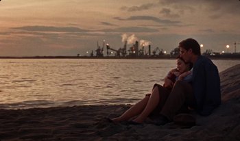 Movie still from “Martin Eden” (2019), directed by Pietro Marcello – Two people sitting on the beach at sunset; Wide shot, High angle