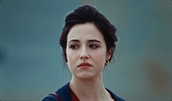 Movie still from “Martin Eden” (2019), directed by Pietro Marcello – A young woman with dark brown hair wearing a blue sweater; Close Up shot, Over the shoulder angle