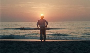 Movie still from “Martin Eden” (2019), directed by Pietro Marcello – A man standing on the beach looking out at the sunset; Wide shot, Low angle