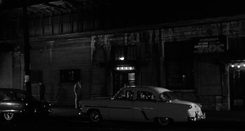 Movie still from “Marty” (1955), directed by Delbert Mann – An old car parked in front of a building at night; Extreme Wide shot, Low angle