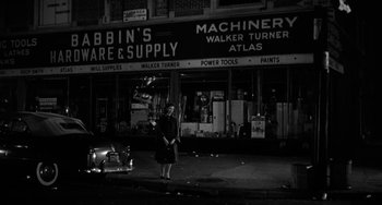 Movie still from “Marty” (1955), directed by Delbert Mann – A woman standing on the side of the road in front of a store; Wide shot, Low angle