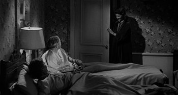 An old photo of a woman standing next to an older woman in a bed