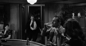 Movie still from “Marty” (1955), directed by Delbert Mann – A man drinking a beer while another man walks by; Medium shot, Over the shoulder angle
