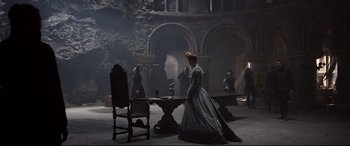 Movie still from “Mary Queen of Scots” (2018), directed by Josie Rourke – A woman dressed in a period dress standing in front of a table with an umbrella; Wide shot, High angle