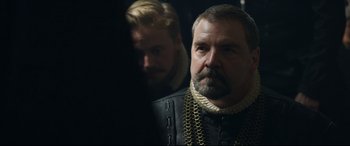 Movie still from “Mary Queen of Scots” (2018), directed by Josie Rourke – A man with a beard wearing a black and white outfit; Close Up shot, Over the shoulder angle
