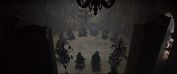 Movie still from “Mary Queen of Scots” (2018), directed by Josie Rourke – A group of people sitting in a circle in front of a chandelier; Wide shot, High angle