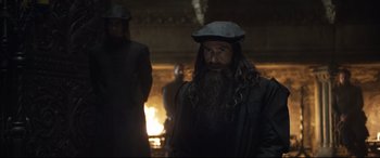 Movie still from “Mary Queen of Scots” (2018), directed by Josie Rourke – A man with long hair and a beard is standing in front of a fire; Medium shot, Over the shoulder angle