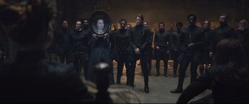 Movie still from “Mary Queen of Scots” (2018), directed by Josie Rourke – A group of people standing around a woman holding a plate; Wide shot, Over the shoulder angle