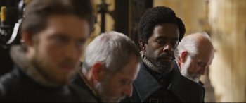 Movie still from “Mary Queen of Scots” (2018), directed by Josie Rourke – A man with a beard is sitting next to two other men; Close Up shot, Over the shoulder angle