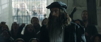 Movie still from “Mary Queen of Scots” (2018), directed by Josie Rourke – A man with long hair and a beard wearing a black hat; Medium shot, Over the shoulder angle